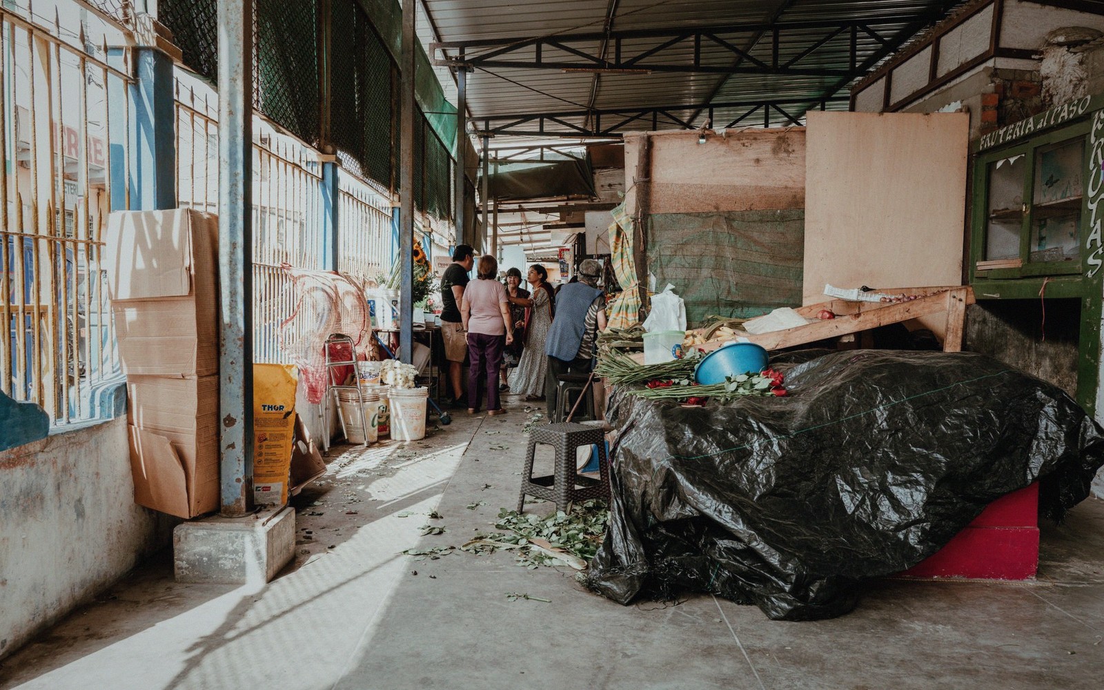 People gather beside covered market stalls and stacked boxes in a covered alleyway