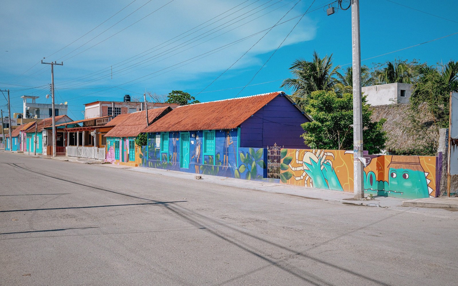 Colorful murals cover a row of houses along a quiet coastal street